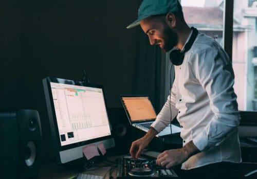 A DJ with headphones plays music on a computer.