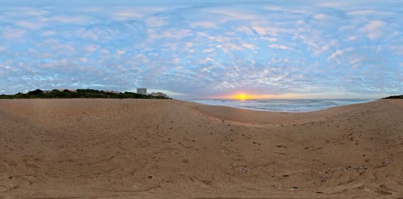 A high dynamic range image (HDRI) from Poly Haven displays an ocean beach with cloudy sky. 