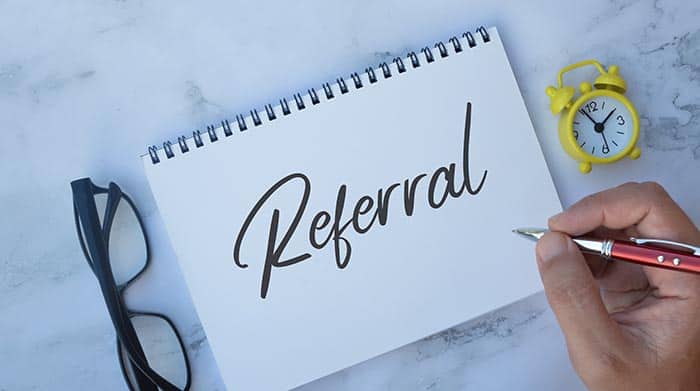 The word "referral" is written on a pad of paper with glasses and a small clock next to it. 